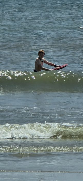 One of the kids catches a wave on the boogie board, riding it in toward shore.
