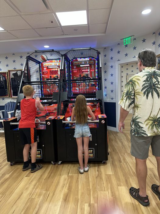 The kids go head-to-head on side-by-side basketball arcade machines while the rest of the family looks on.