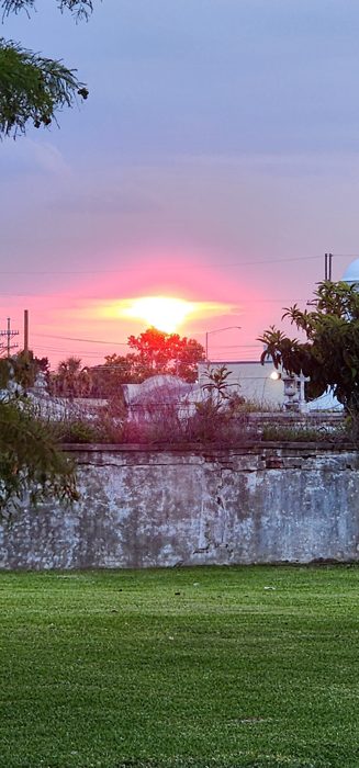 The sun drops fiery red behind the cemetery wall in an unforgettable New Orleans dusk.