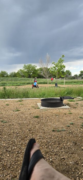 Toes-up by the fire ring, soaking in the view across the grassy campground at Boyd Lake.
