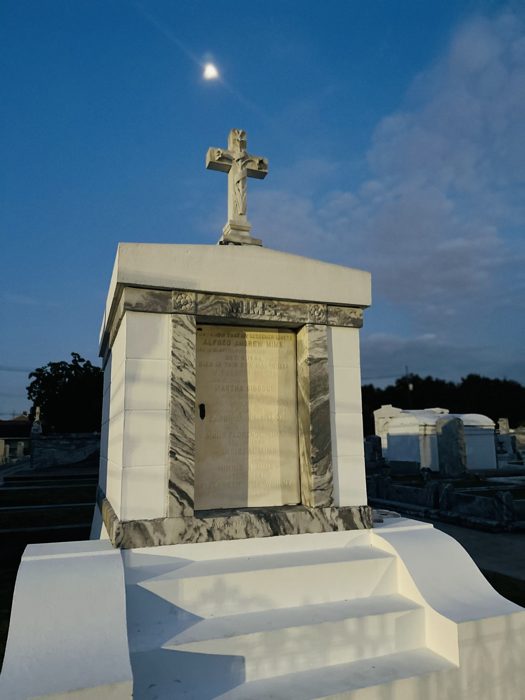 A cross-topped marble tomb catches the last light against a clear evening sky.
