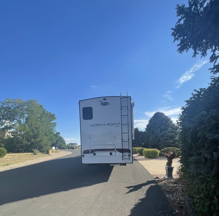 Pulling the fifth wheel down a tree-lined campground lane under a deep blue sky.