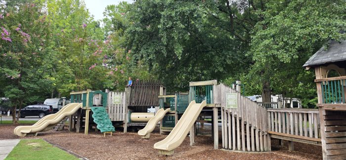 One of the kids climbs high on the playground structure while the quiet pool and RVs wait below.
