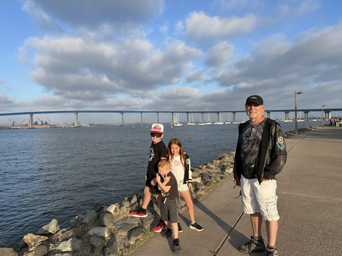 The family pauses along the bayfront walkway with the Coronado Bridge sweeping across the water behind them.