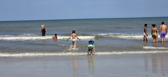 A packed beach comes alive as the kids splash out into the surf among the other families.