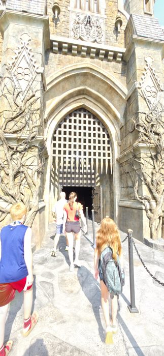 The family passes under a towering stone archway into Frankenstein's castle at Universal's Dark Universe.