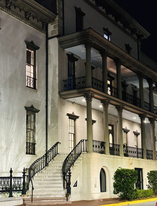 A grand Southern mansion with its sweeping staircase glowing at night.
