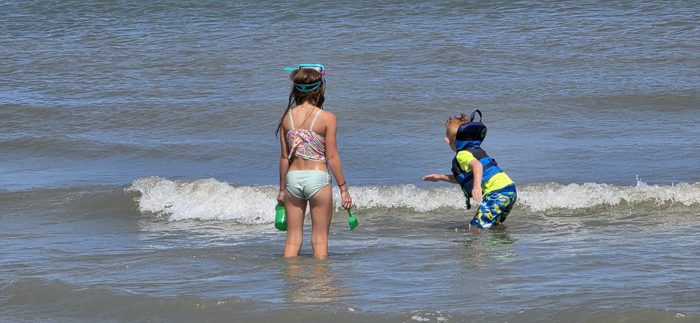 The kids pause together in the surf, buckets in hand, watching the next wave roll in.