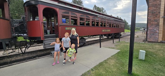 The kids gather alongside the maroon coaches of the 1880 Train before we climb aboard.