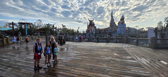 The kids pose on the empty boardwalk with the dragon-topped peaks of Berk rising behind them.